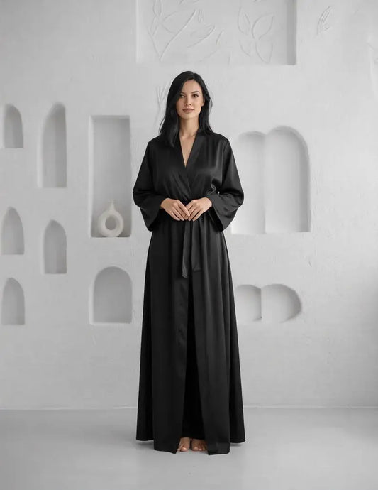 Woman wearing a black robe standing against a white wall with geometric patterns. 